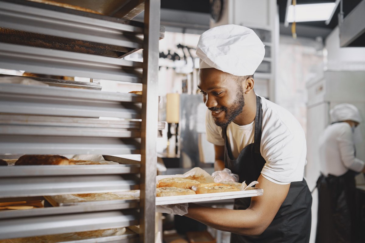 A smiling baker sliding a tray of freshly baked bread onto a rack in a bakery