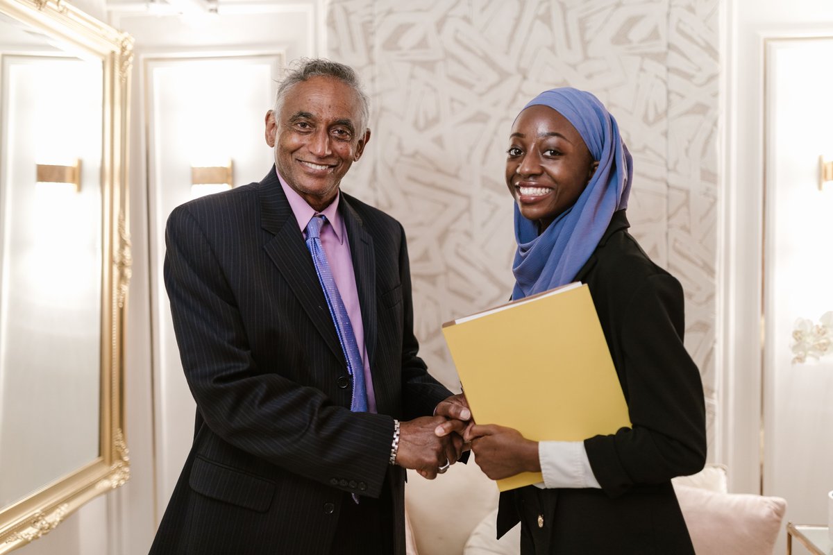 A loan officer shaking hands with a young businesswoman holding a yellow folder