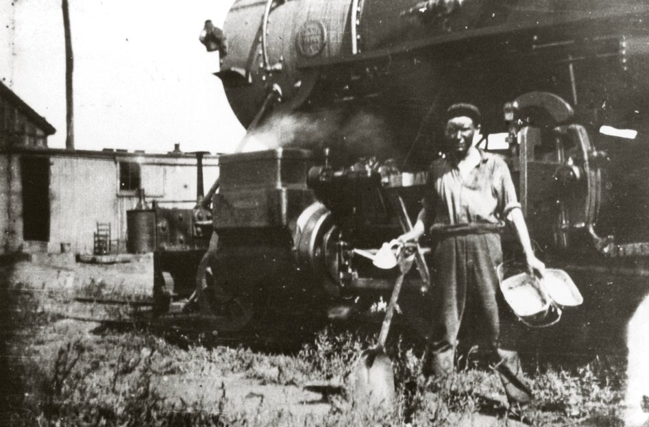 Harland Sanders as a young railroad worker standing beside a steam locomotive, around 1915
