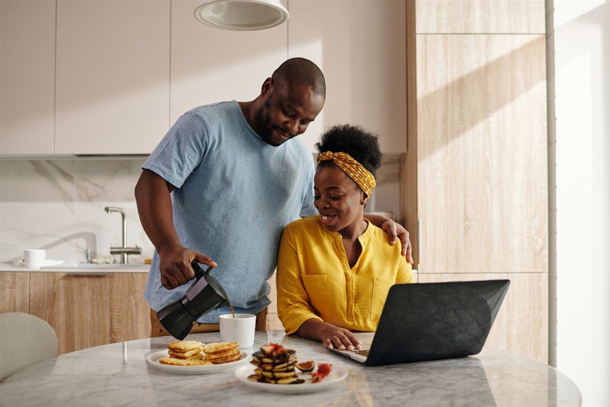 A couple enjoying breakfast and coffee while planning on a laptop in their kitchen