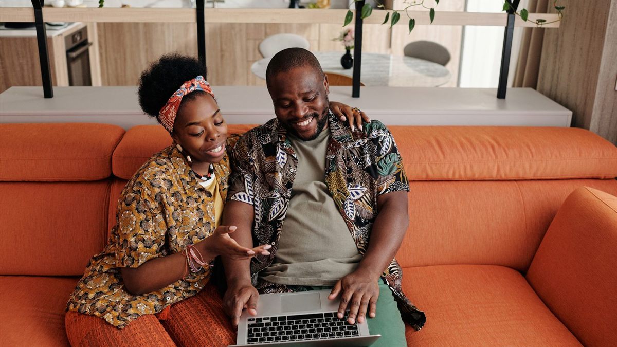 A smiling couple on an orange sofa planning their money together on a laptop