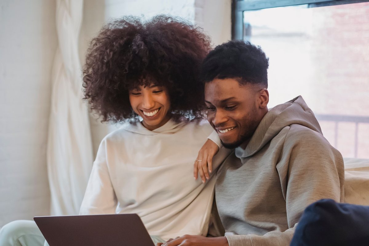 A smiling young couple sitting together on a sofa, planning on a laptop