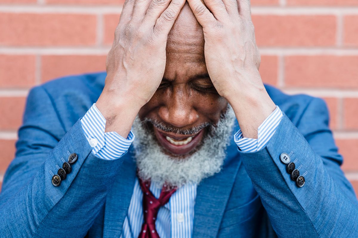 A stressed man in a blue suit holding his head in both hands
