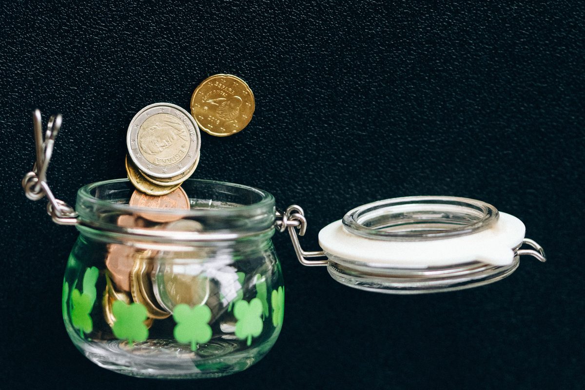 Coins dropping into a glass savings jar