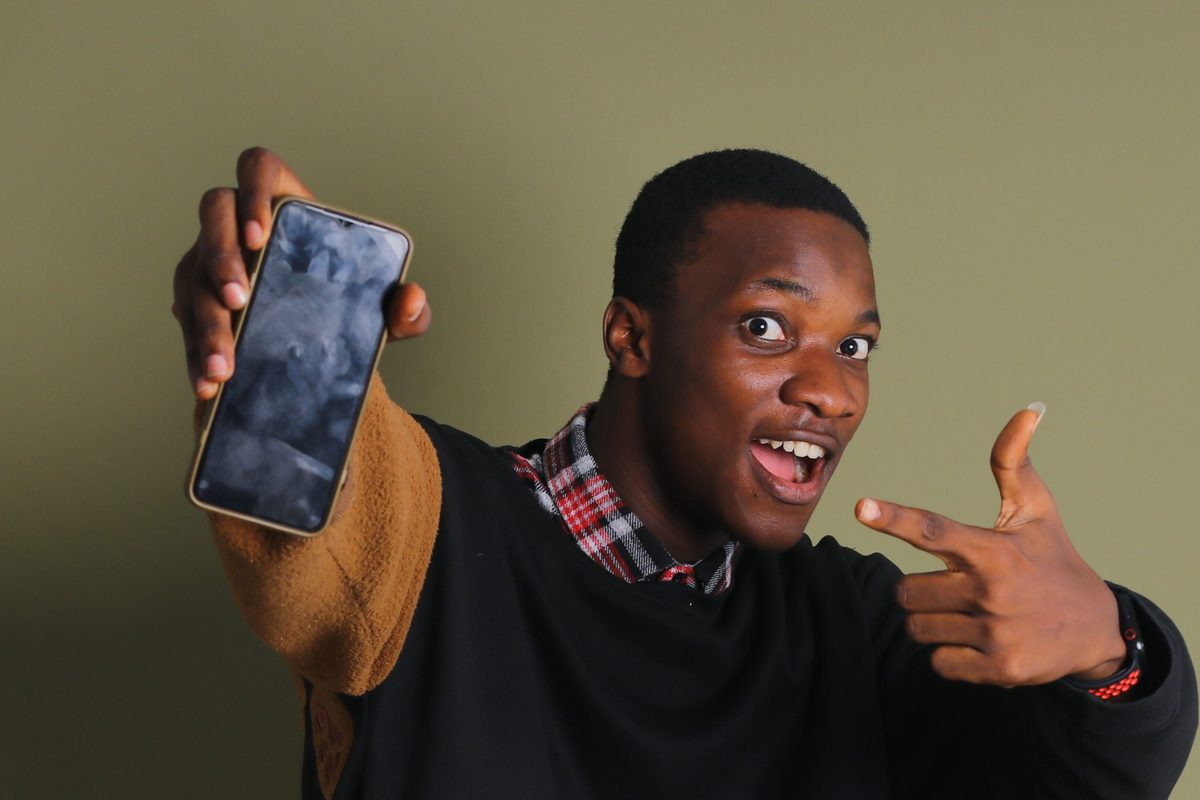 A young man smiling and pointing at his smartphone screen