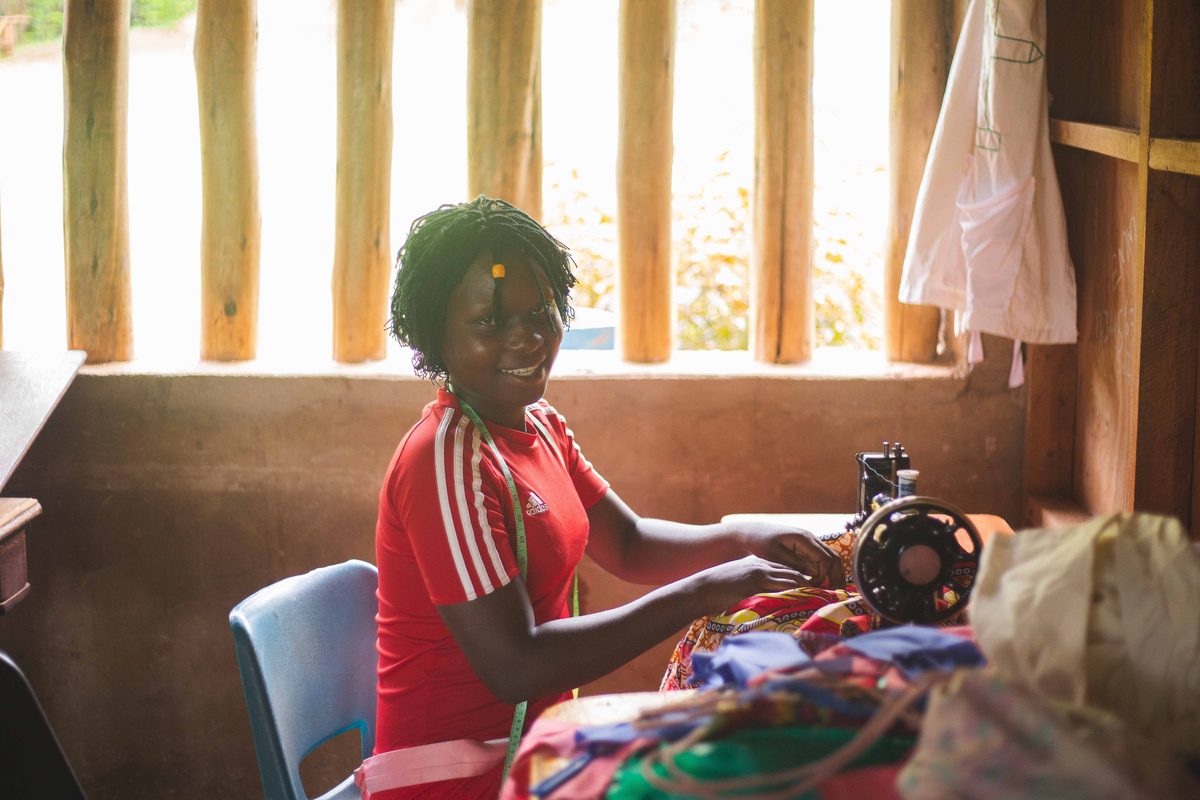 A smiling tailor at her sewing machine with colourful kitenge fabric in a small workshop